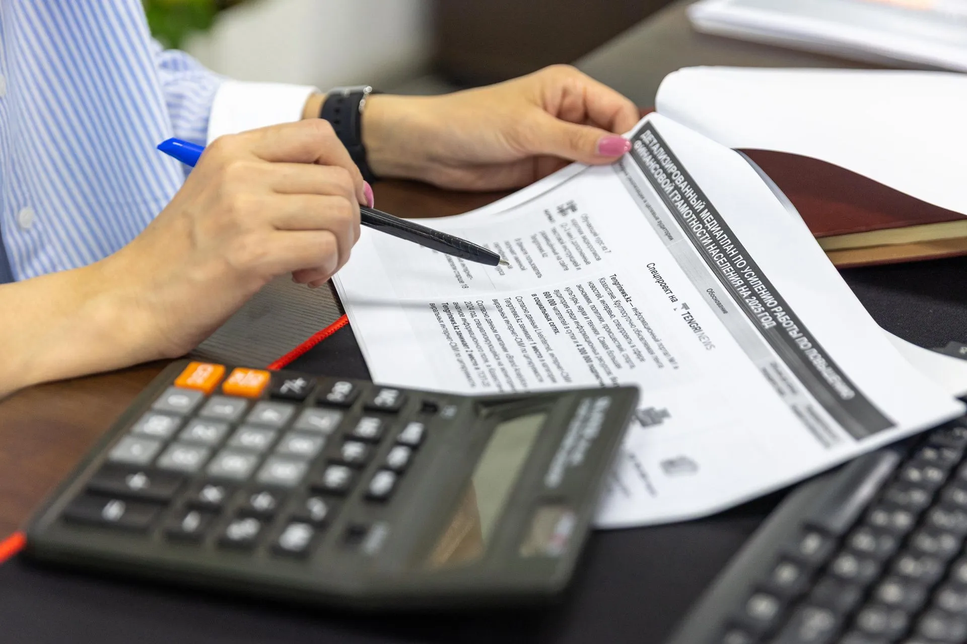 Pessoa revisando documentos com caneta, ao lado de uma calculadora